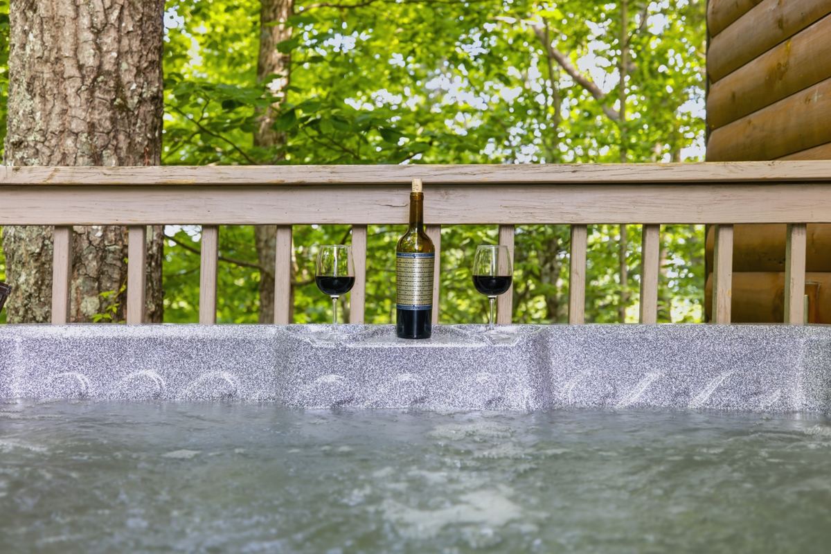 A bottle of red wine and two glasses on the edge of the hot tub